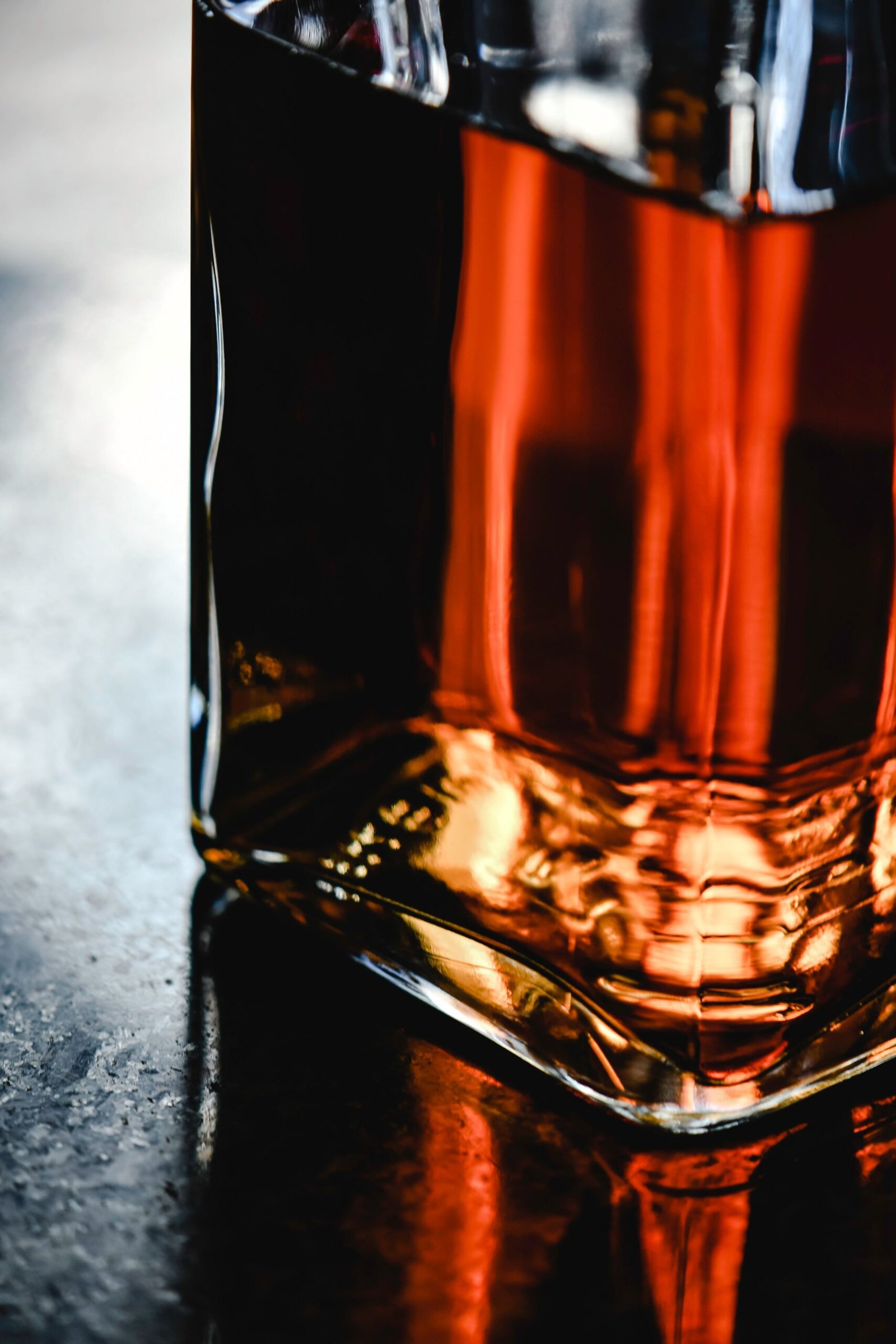 Artistic close-up of a liquor bottle with warm reflections on a textured surface.